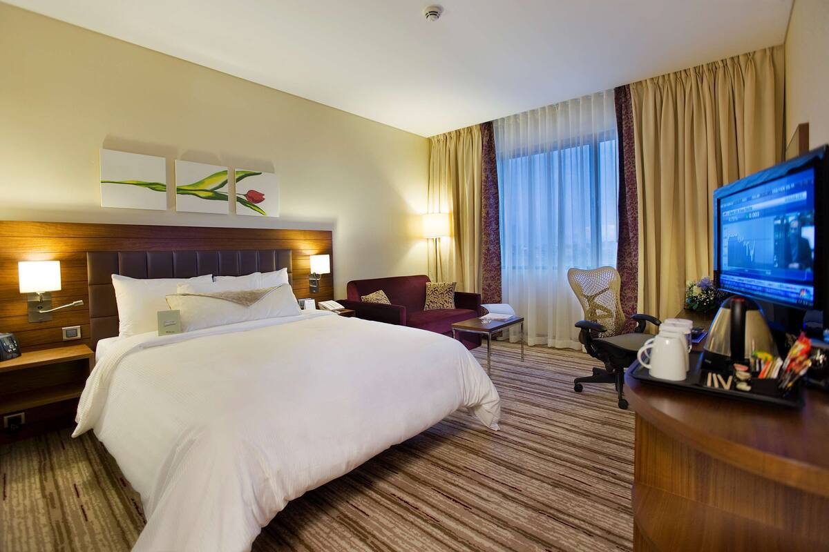 A hotel room with a large bed, a desk with a computer, a TV, and a seating area with a couch and chair.