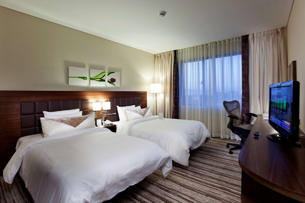 A hotel room with two beds, a desk with a computer, a lamp, and a TV.