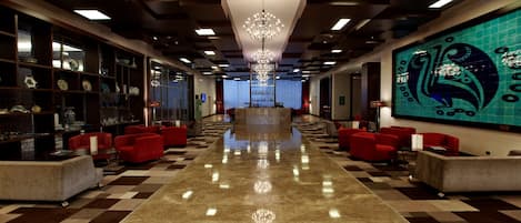 Un vestíbulo de hotel con piso a cuadros, asientos rojos, un candelabro y un mural grande en la pared.