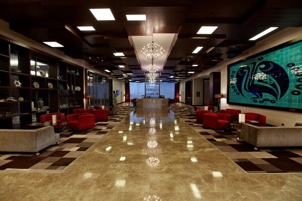A hotel lobby with a checkered floor, red seating, a chandelier, and a large wall mural.