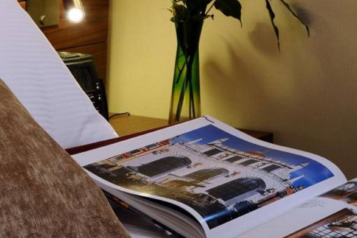 A hotel room with a bed, a bedside lamp, a vase with flowers, and a magazine on the bed.