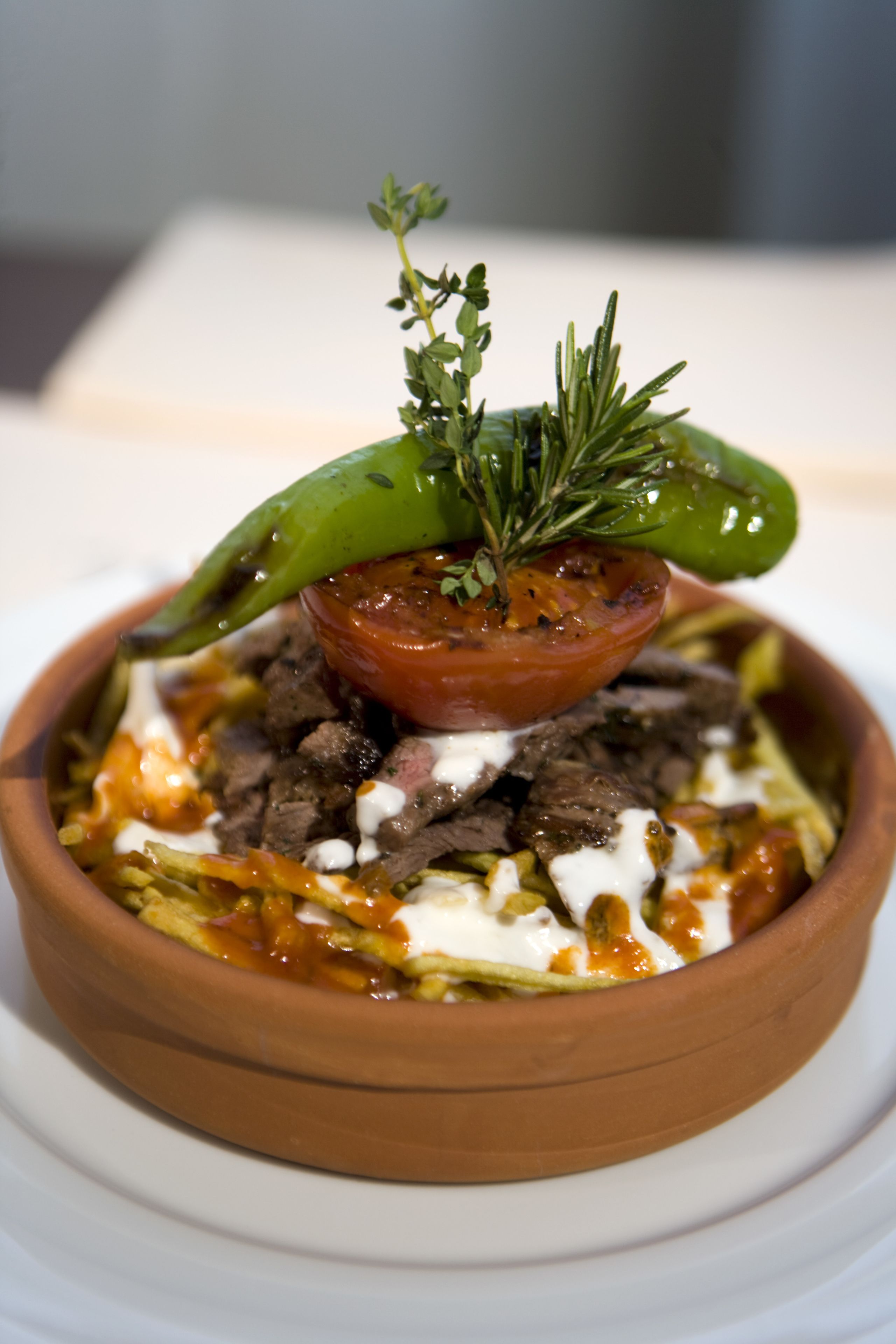 Un plato de comida con un chile verde, un tomate y una ramita de hierba encima.