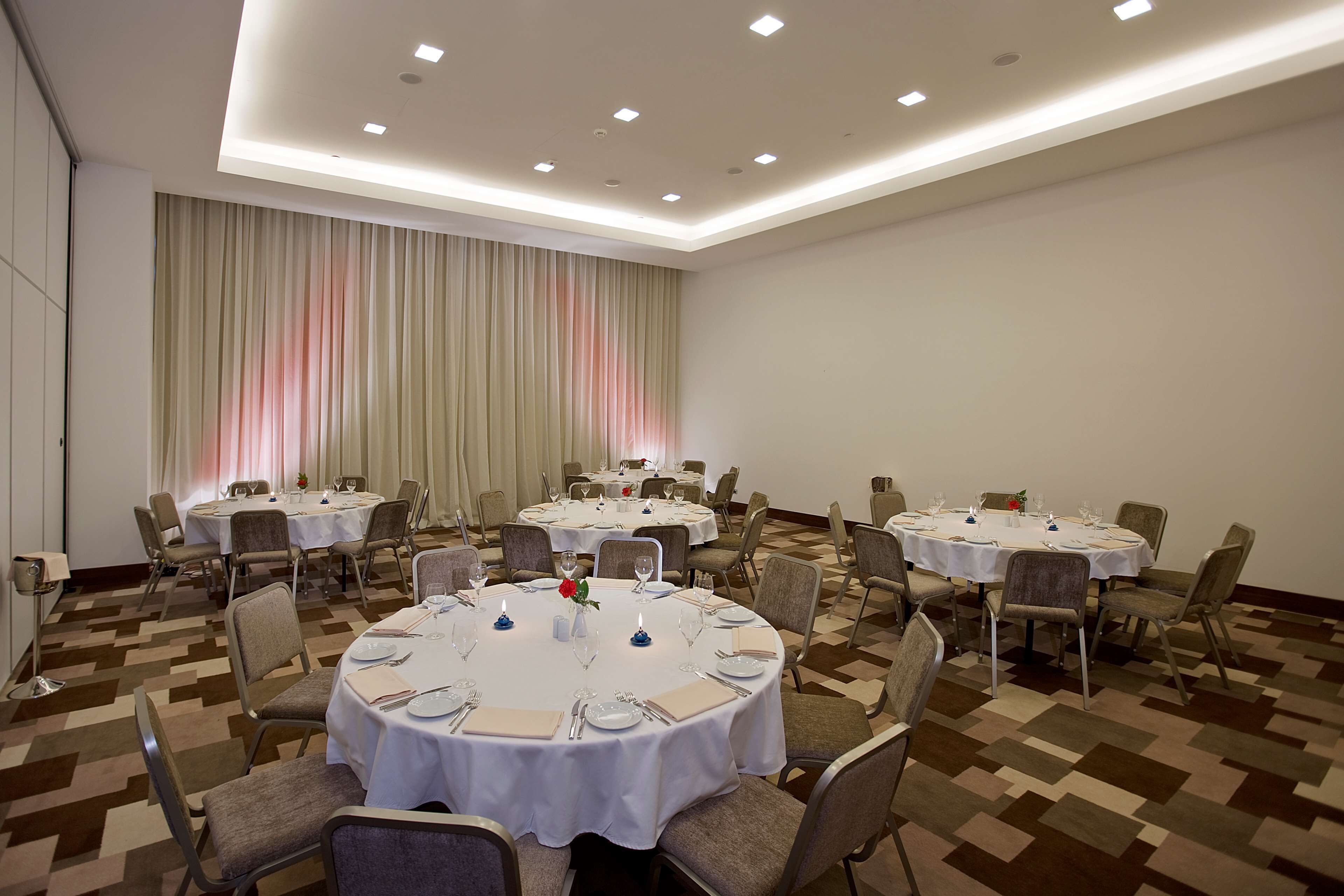 A conference room with multiple round tables, each set with white tablecloths, chairs, and dining essentials.