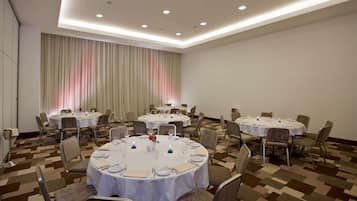 A conference room with multiple round tables, each set with white tablecloths, chairs, and dining essentials.