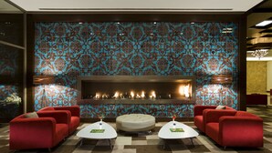 A lobby with a patterned wall, a fireplace, red sofas, and a checkered floor. - Hilton Garden Inn Kutahya (Kutahya)