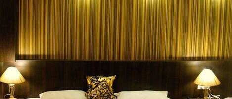 A hotel room with a large bed, two bedside lamps, a patterned pillow, and a dark headboard.