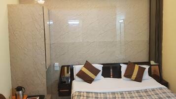 Habitación de hotel con pared de mármol, cama con ropa de cama escocesa y mesita de noche con cafetera y teléfono.