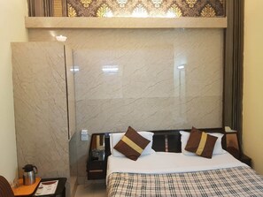 A hotel room with a marble wall, a bed with plaid bedding, and a nightstand with a coffee pot and phone. - Hotel CJ International (Amritsar)
