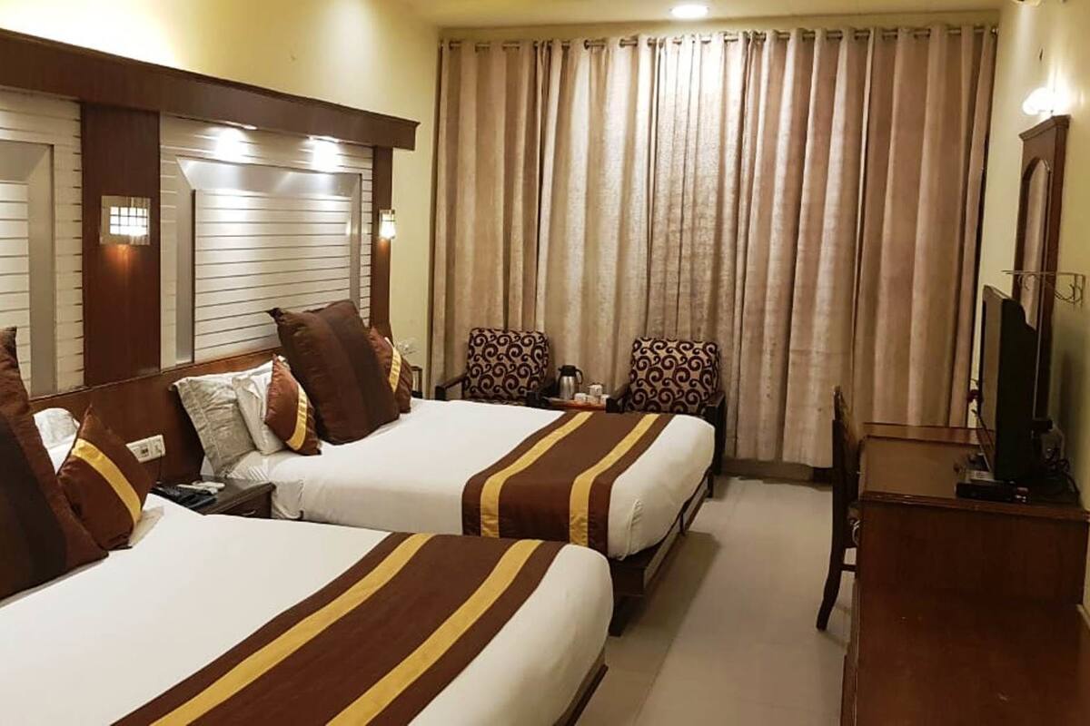 A hotel room with two beds, each with striped bedding and multiple pillows. There is a desk with a television and a lamp.