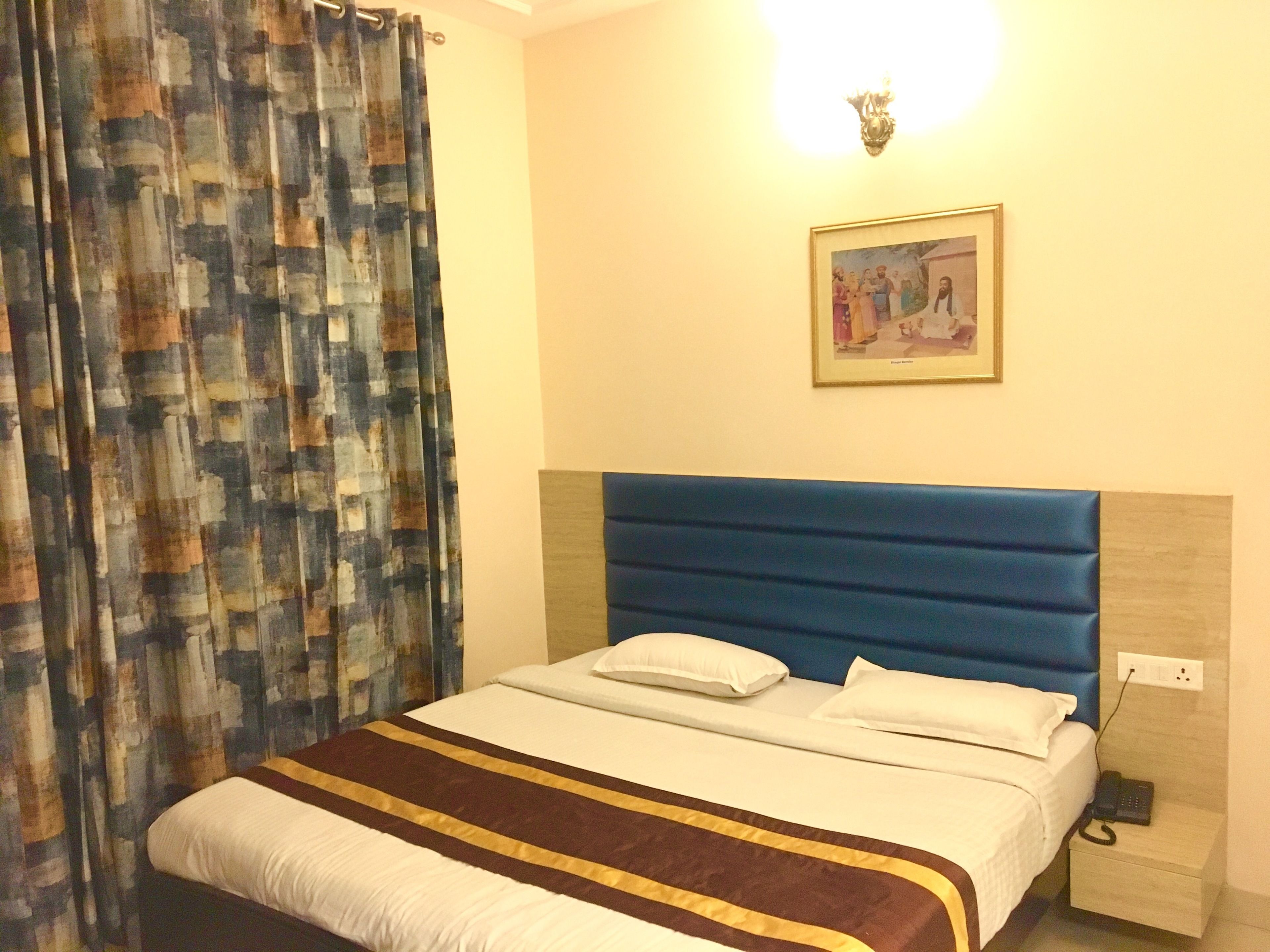 A hotel room with a bed, a nightstand, a lamp, and a painting on the wall.