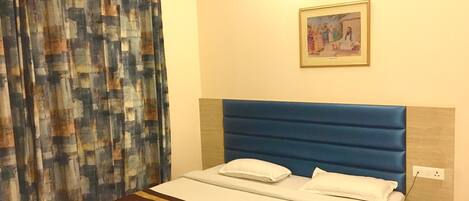 A hotel room with a bed, a nightstand, a lamp, and a painting on the wall.