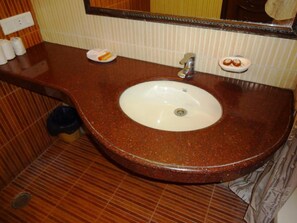 A bathroom with a brown marble sink, a mirror, and a towel rack. - Hotel CJ International (Amritsar)