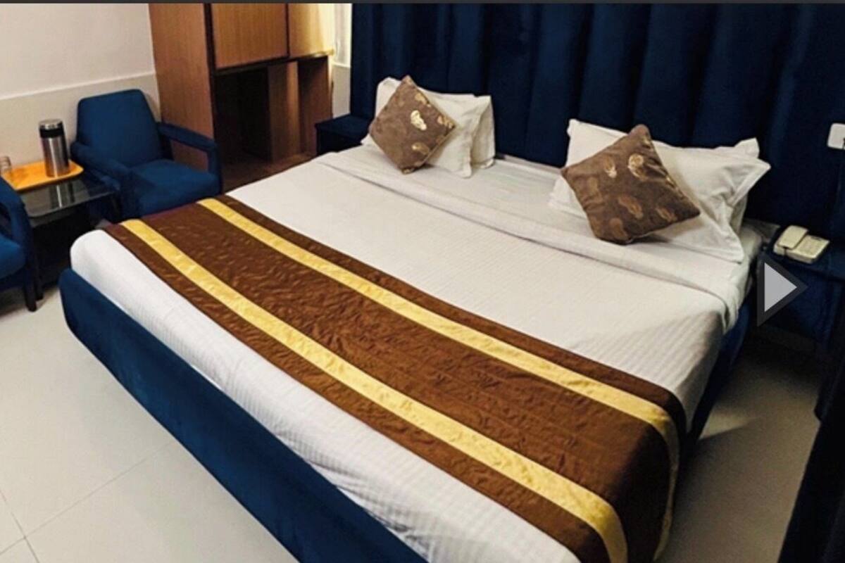 A hotel room with a large bed, two blue armchairs, a small table with a lamp, and a nightstand with a phone.
