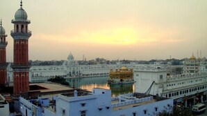 A cityscape with prominent religious buildings, including domed towers and a golden temple, reflecting on a calm body of water. - Hotel CJ International (Amritsar)
