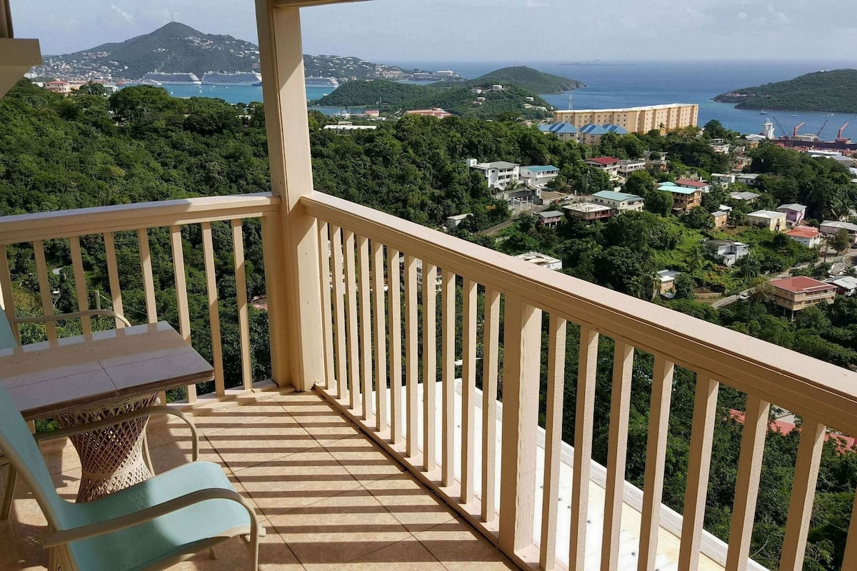 A balcony with a view of a coastal town, a chair, and a small table.