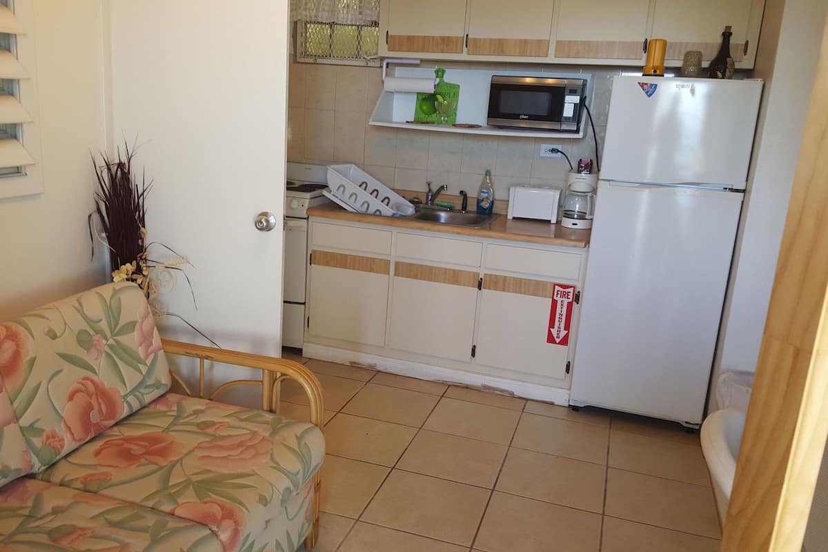 A compact kitchen with a microwave, refrigerator, and sink. There's a floral sofa and a door with a fire exit sign.