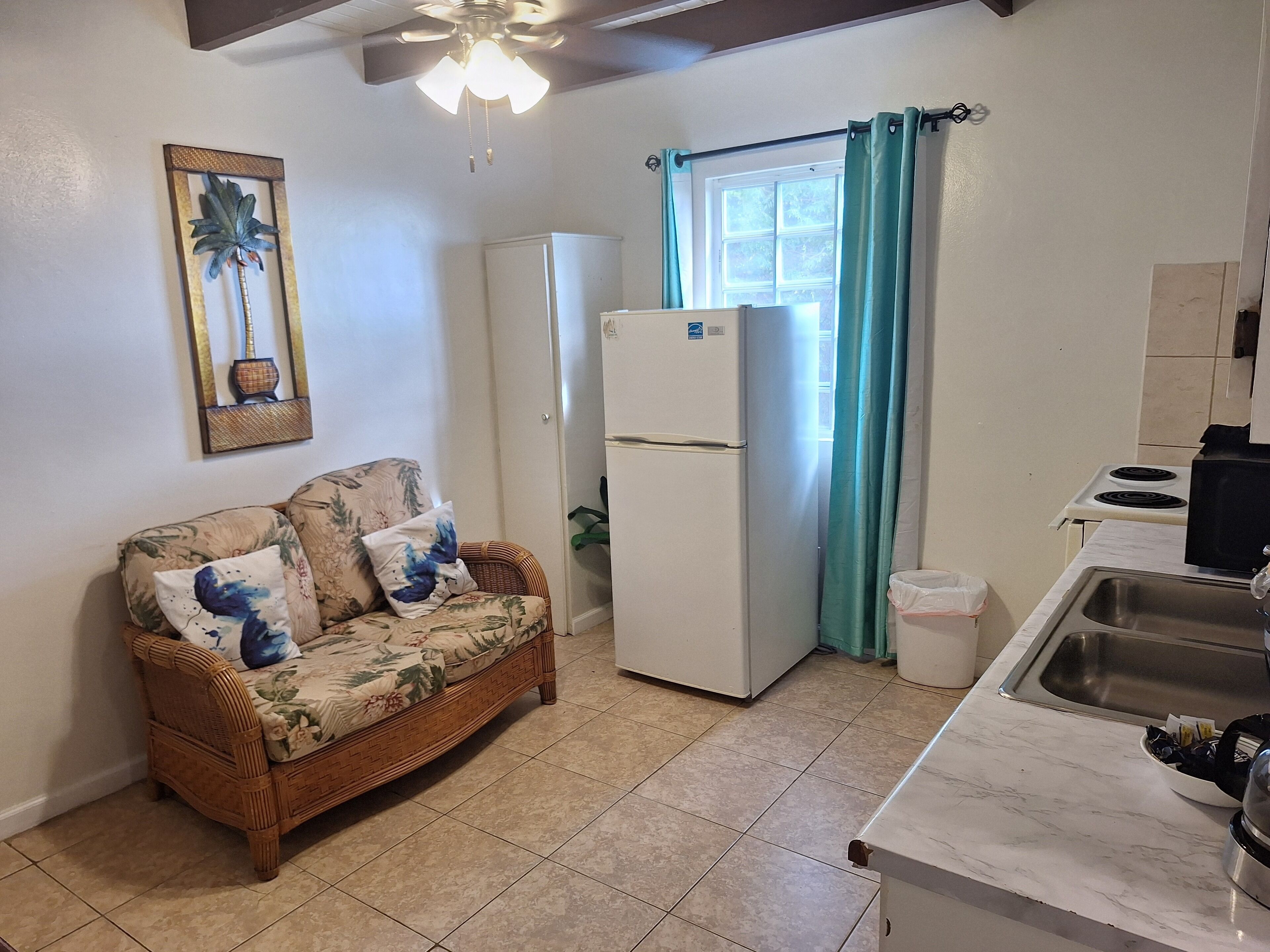 A compact kitchen with a refrigerator, a sink, and a dining area with a wicker sofa.