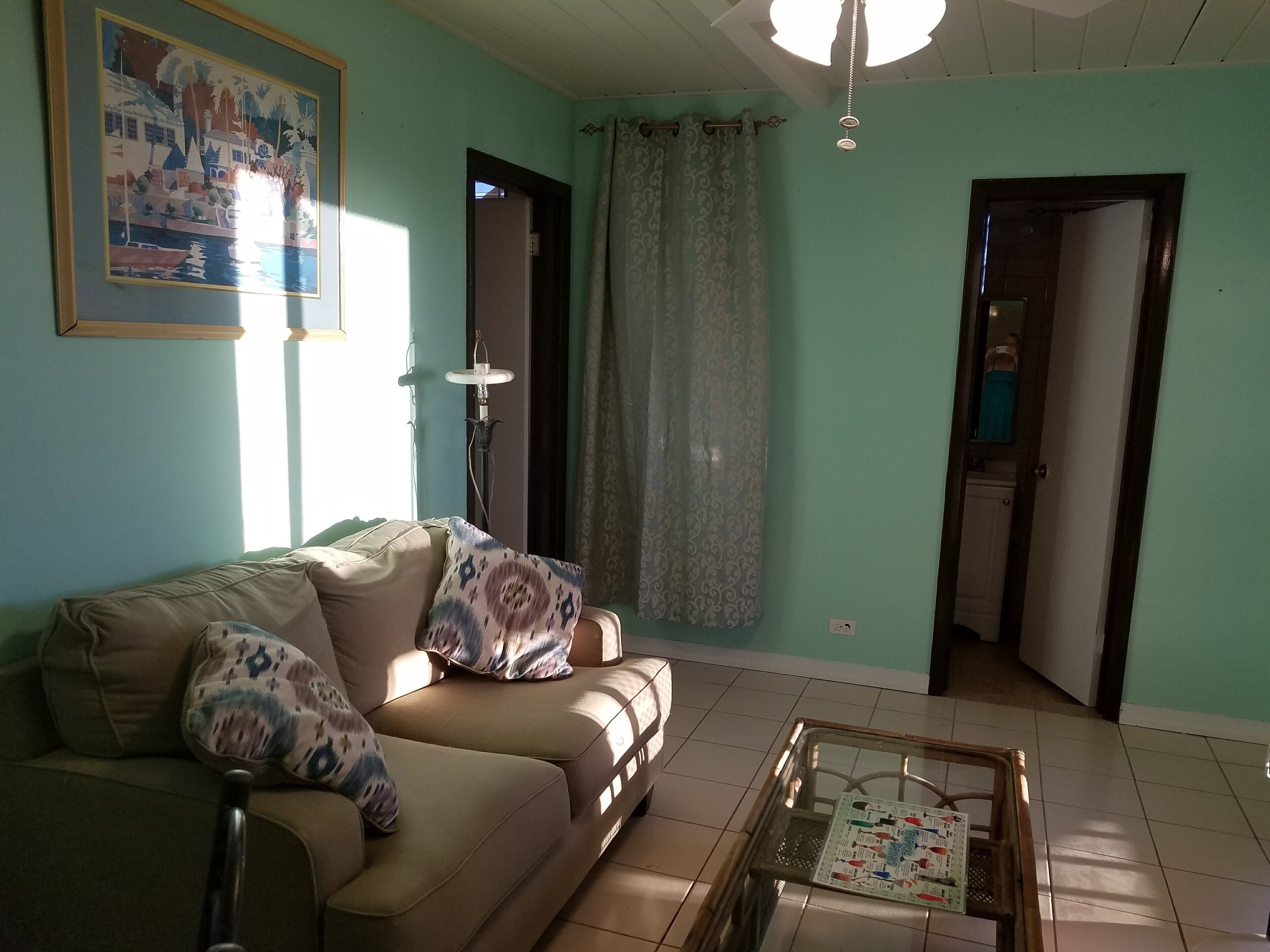 A living room with a sofa, a glass coffee table, and a painting on the wall.