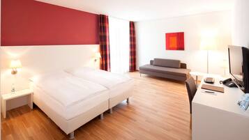 A hotel room with a bed, a sofa, a desk with a computer, and a TV.