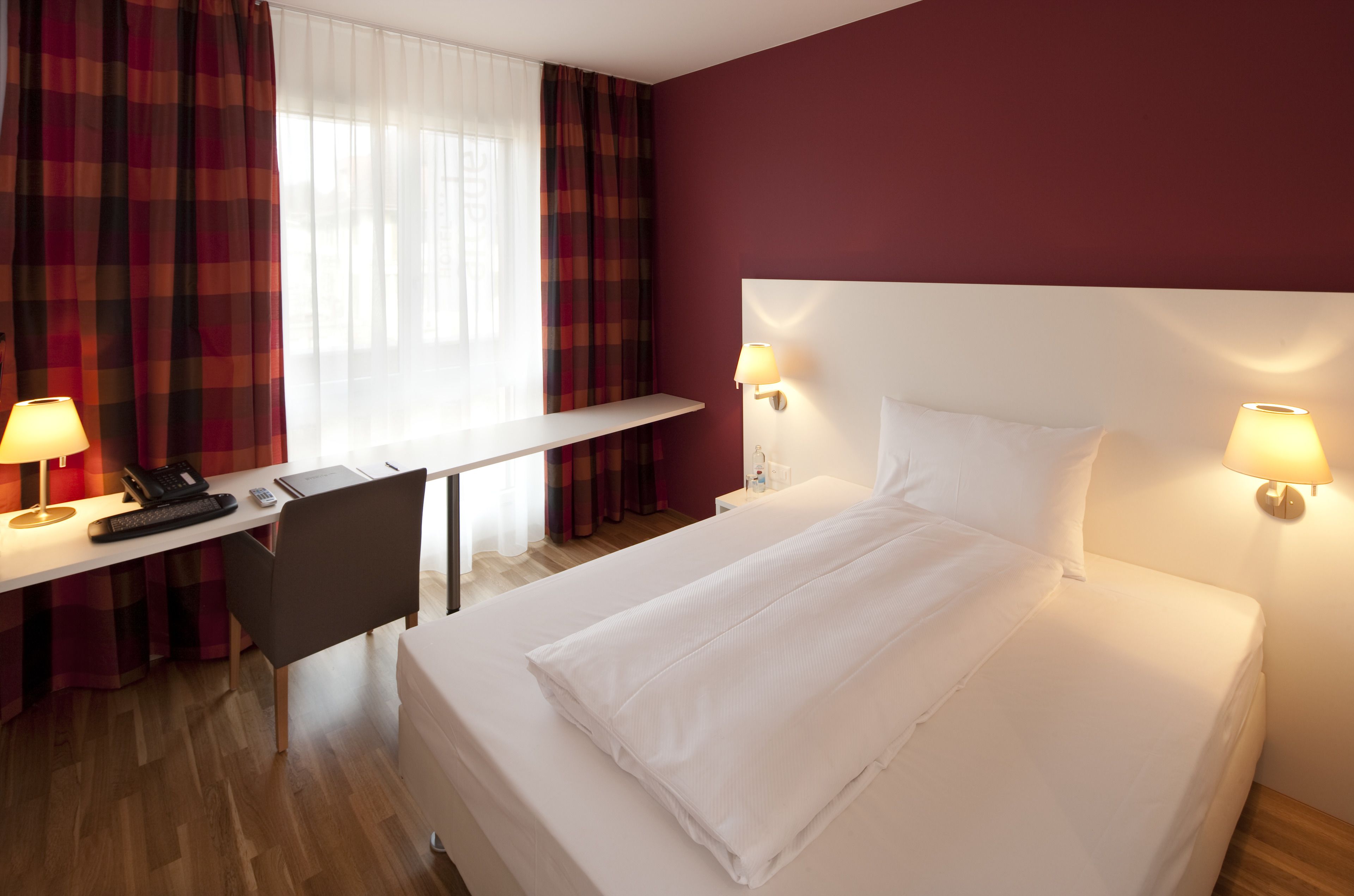Una habitación de hotel con cama, escritorio, silla y dos lámparas de noche.