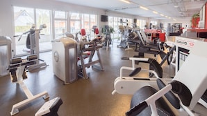 A gym with various exercise equipment, large windows, and a visible treadmill. - Hotel Arcade (Sins)