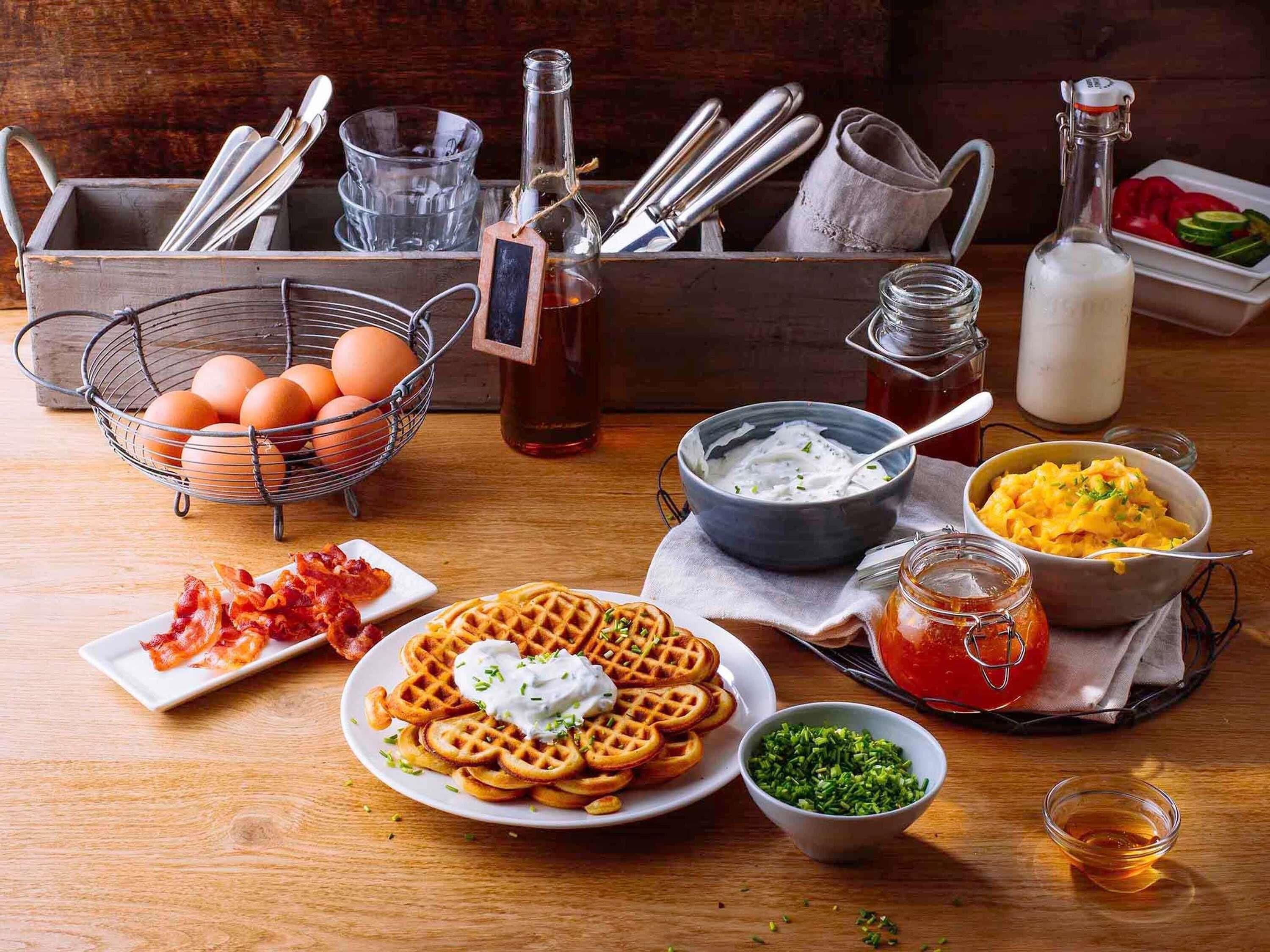 A breakfast setting with waffles, eggs, bacon, yogurt, and condiments.