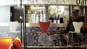 A bar area with modern chairs, a counter with various bottles, and a wall with abstract line art.