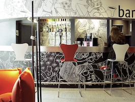 Una zona de bar con sillas modernas, una barra con diferentes botellas y una pared con arte lineal abstracto.