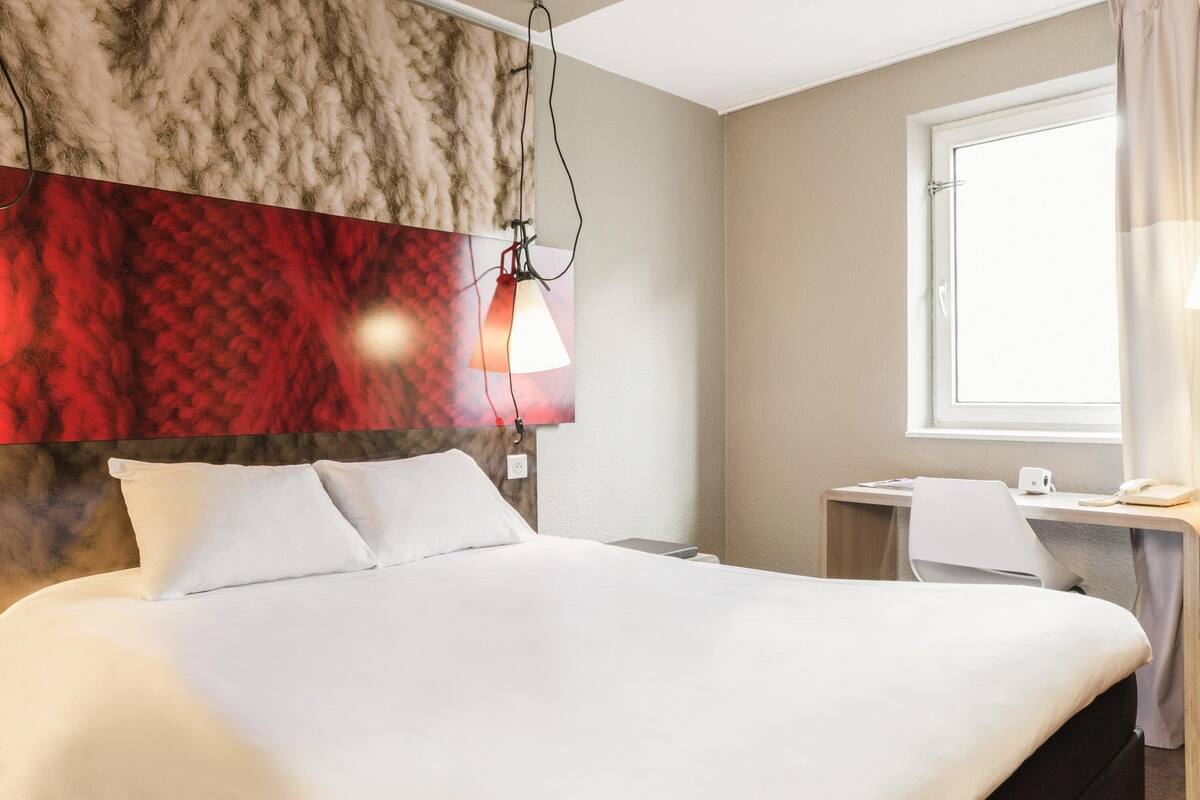 A hotel room with a large bed, a desk with a computer, and a window with curtains.