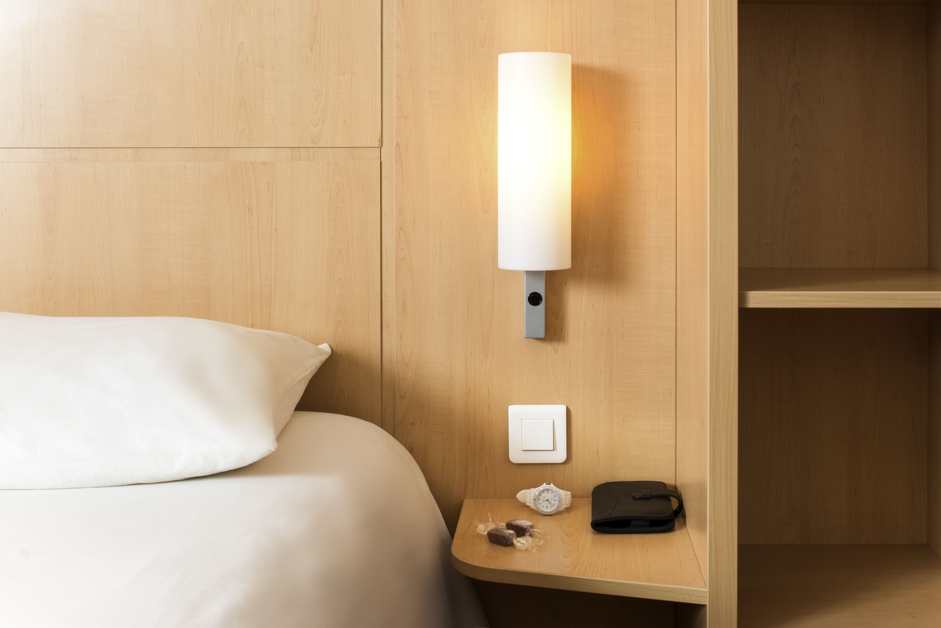 Una habitación de hotel con una cama, una mesita de noche con una lámpara, un teléfono y un reloj.
