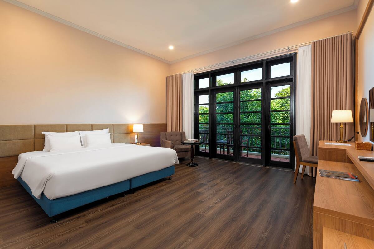 Habitación de hotel con una cama grande, un escritorio, una silla y vistas a zonas verdes por la ventana.