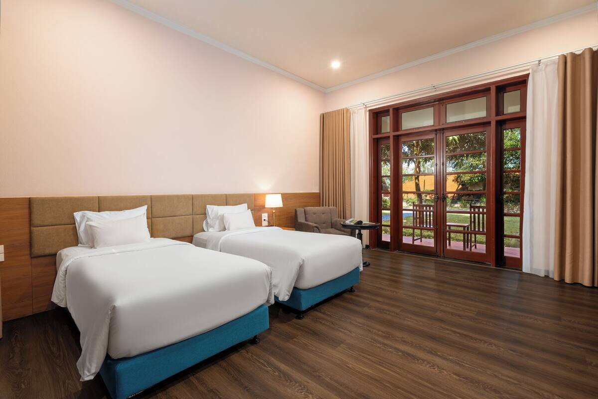 Habitación de hotel con dos camas, piso de madera, un ventanal grande con cortinas y vistas al exterior.