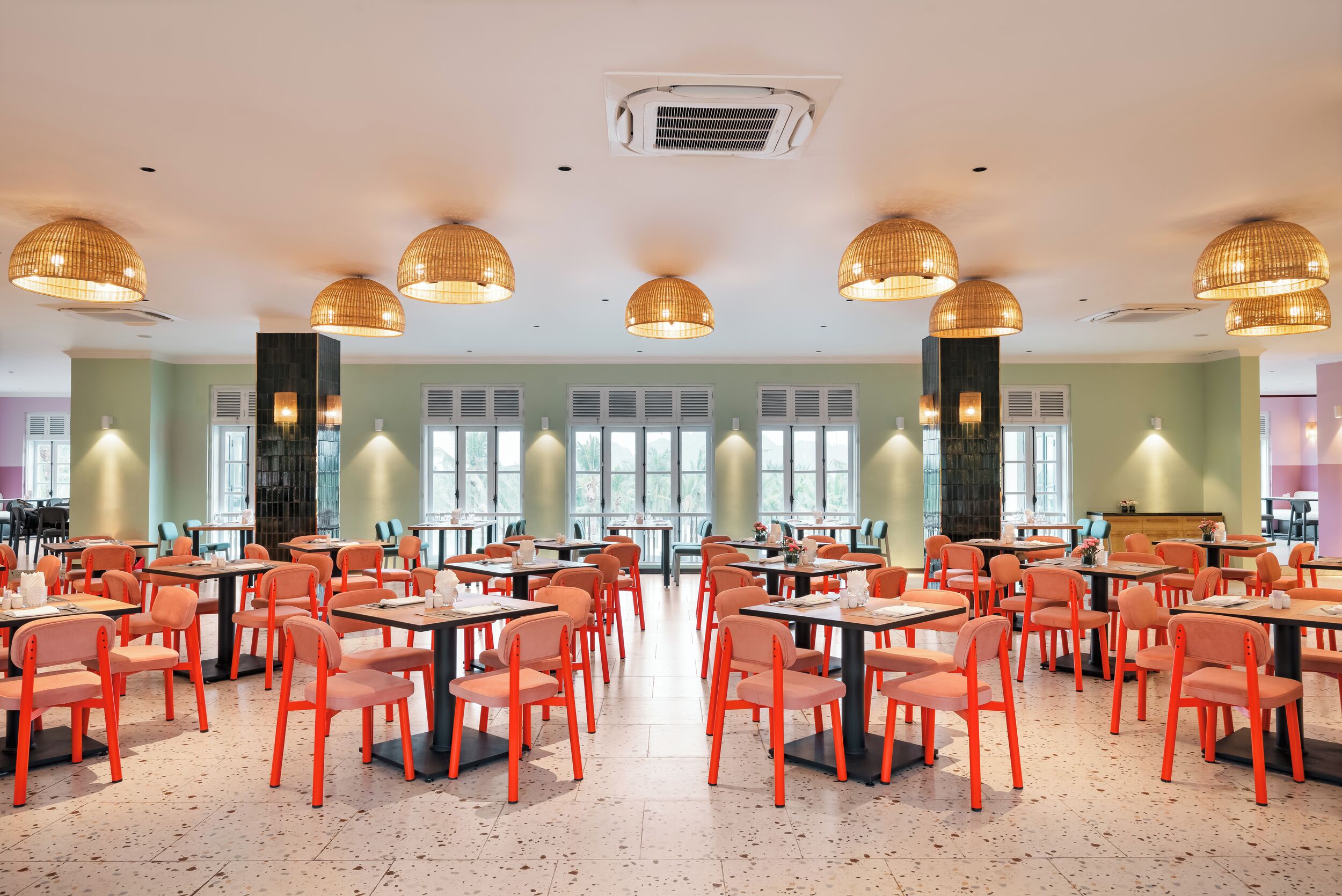 A spacious dining area with multiple tables and chairs, large windows, and decorative hanging lights.