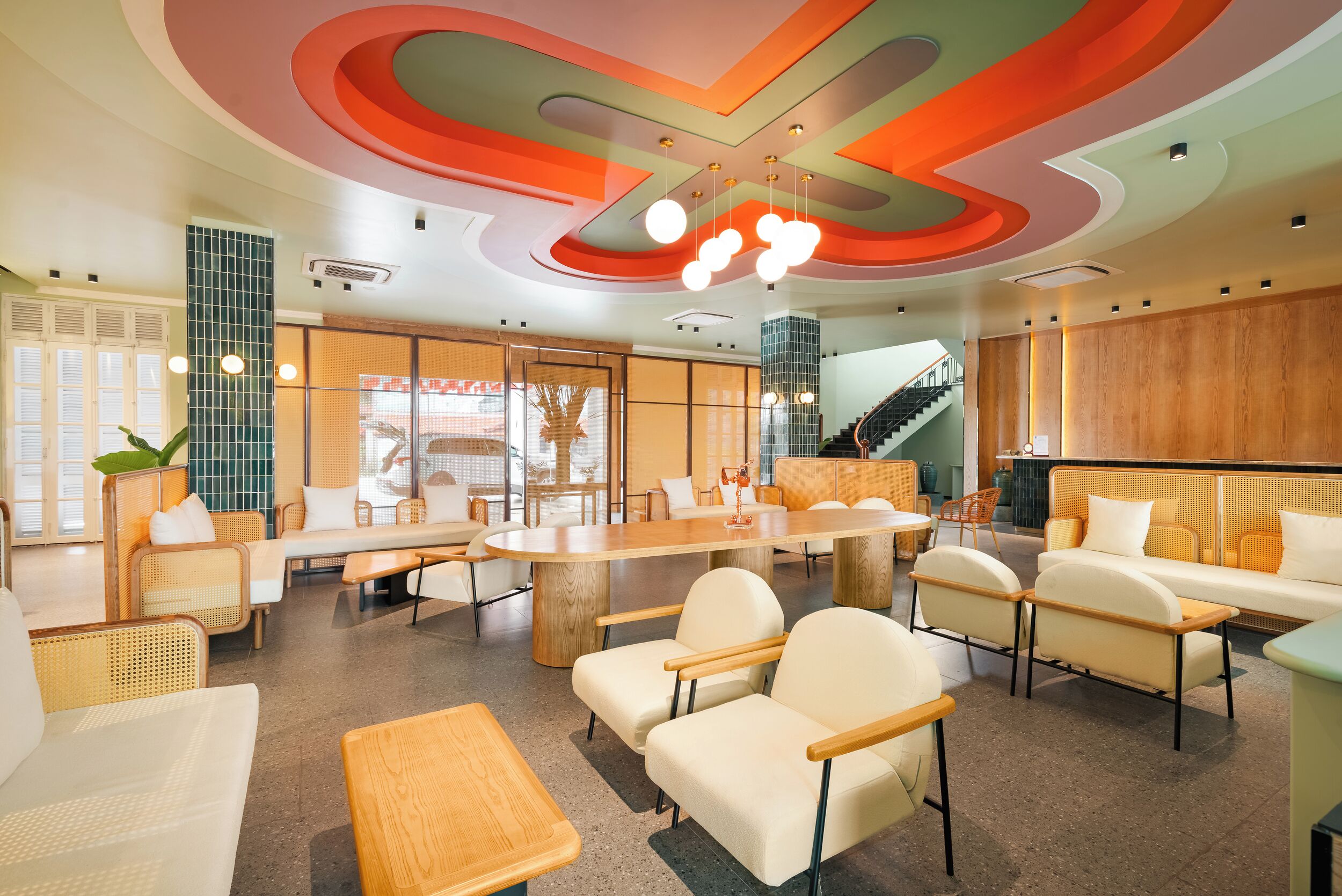 A modern lounge area with a large wooden table, comfortable seating, and a staircase in the background.