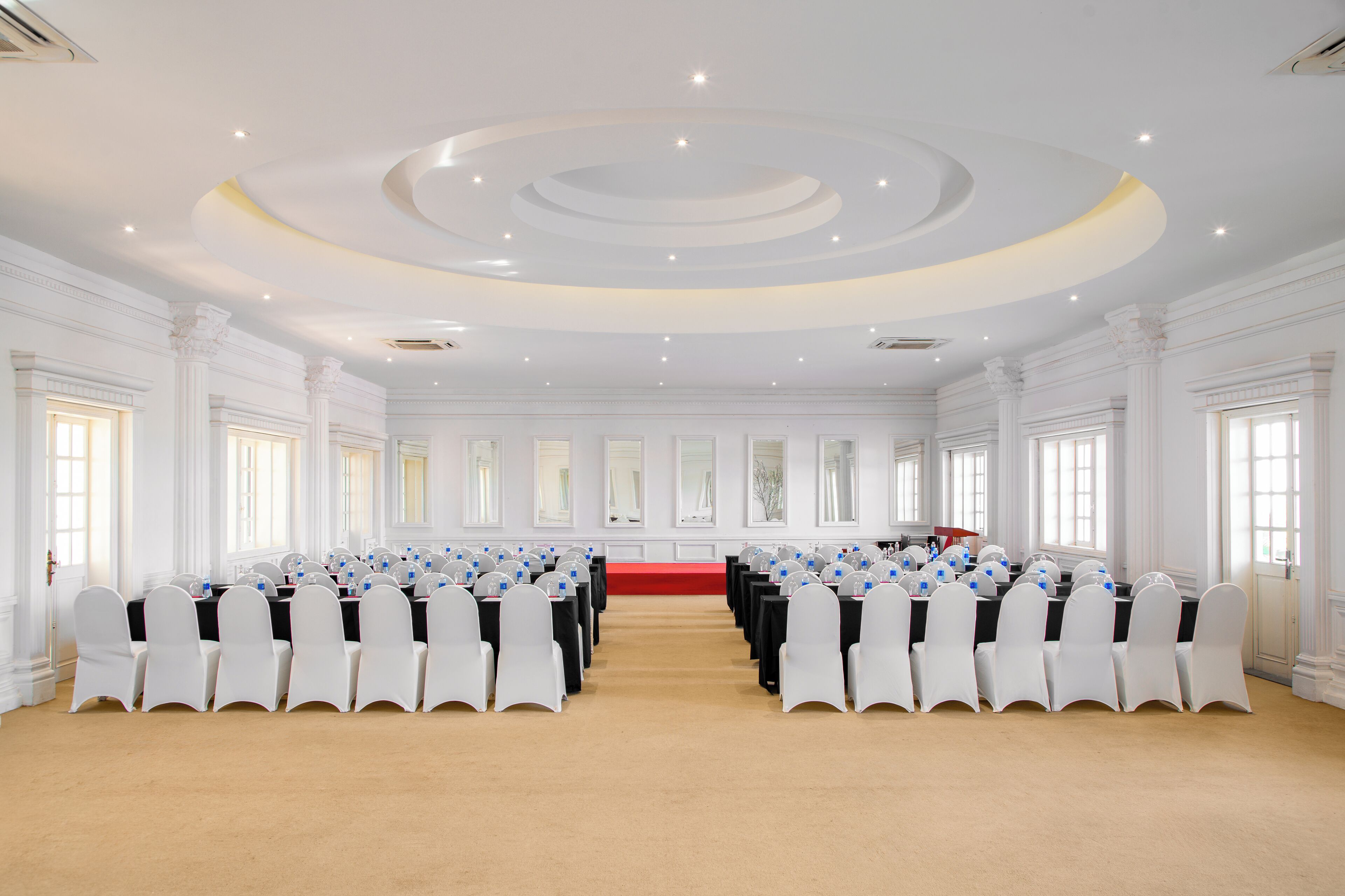 A large conference room with white chairs, a central table, and a red carpet.
