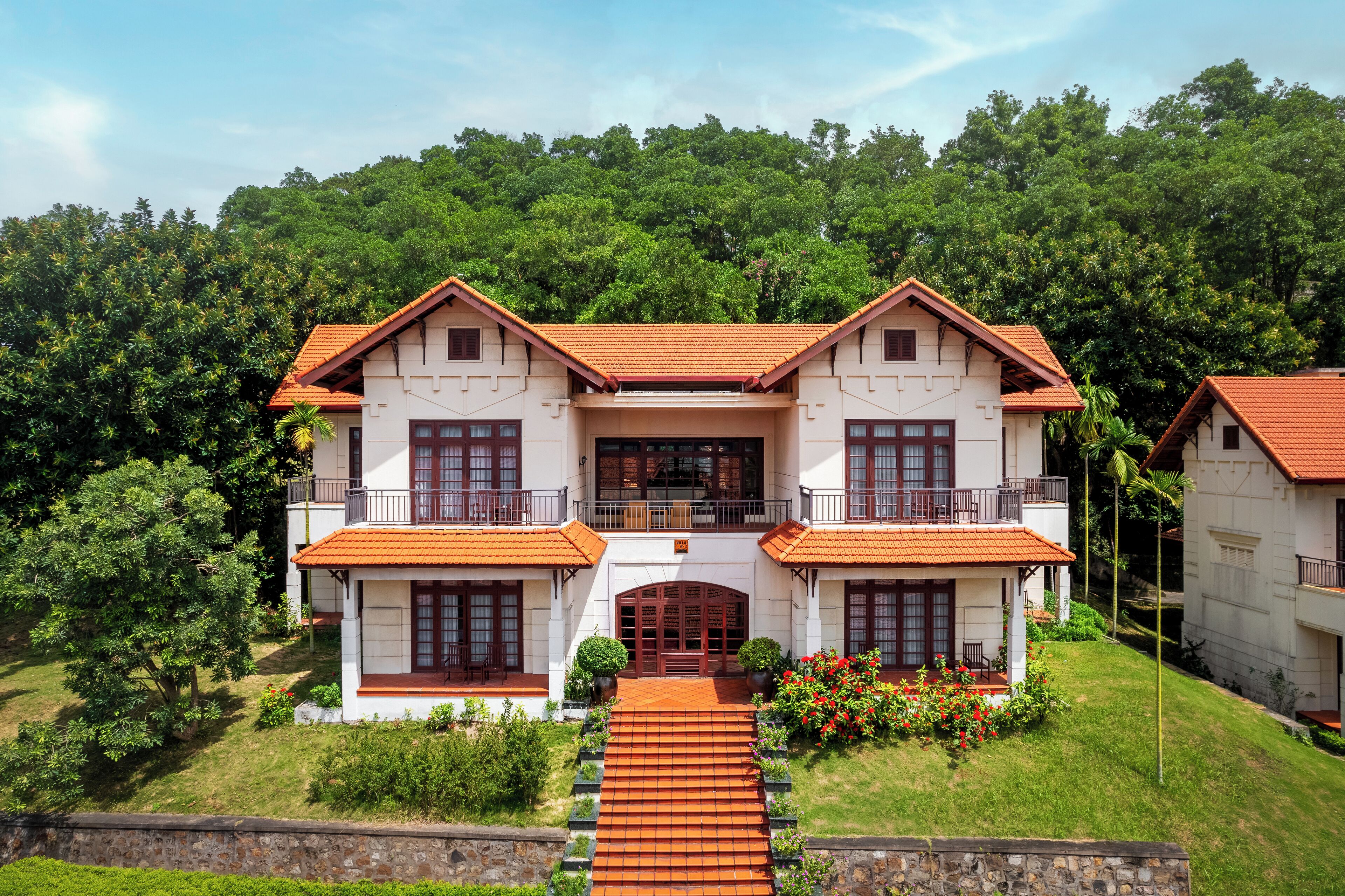 A two-story house with a red-tiled roof, a central entrance, and a balcony on the upper floor.