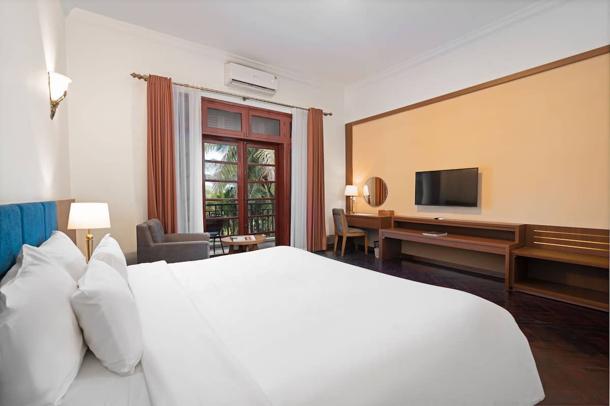 Una habitación de hotel con una cama grande, un escritorio con silla, televisión y ventana con cortinas.