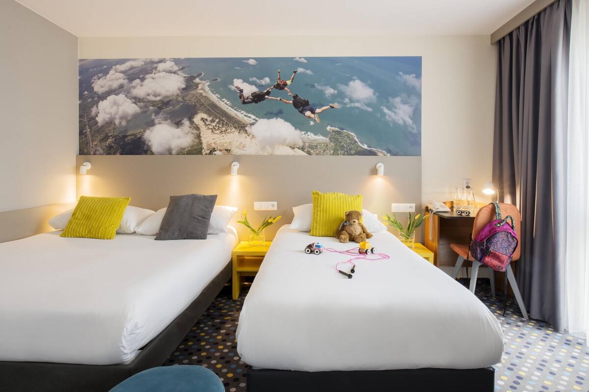 Een hotelkamer met twee bedden, een bureau en een groot wanddecor van parachutisten.