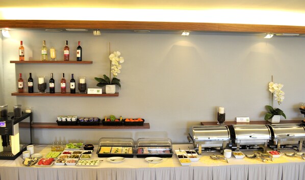 A buffet setup with various food items, a coffee machine, and a selection of wines on shelves. - ibis Styles Warszawa West (Ozarow Mazowiecki)
