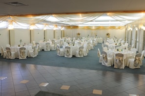 Un salón de banquetes con mesas redondas, manteles blancos y sillas cubiertas de blanco.