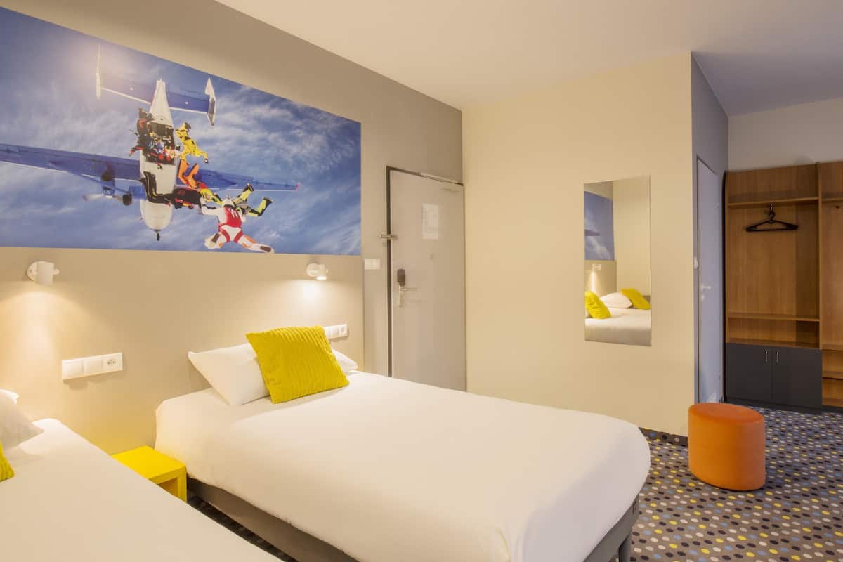 Een hotelkamer met een bed, een tafeltje, een nachtkastje, een spiegel en een kledingkast.