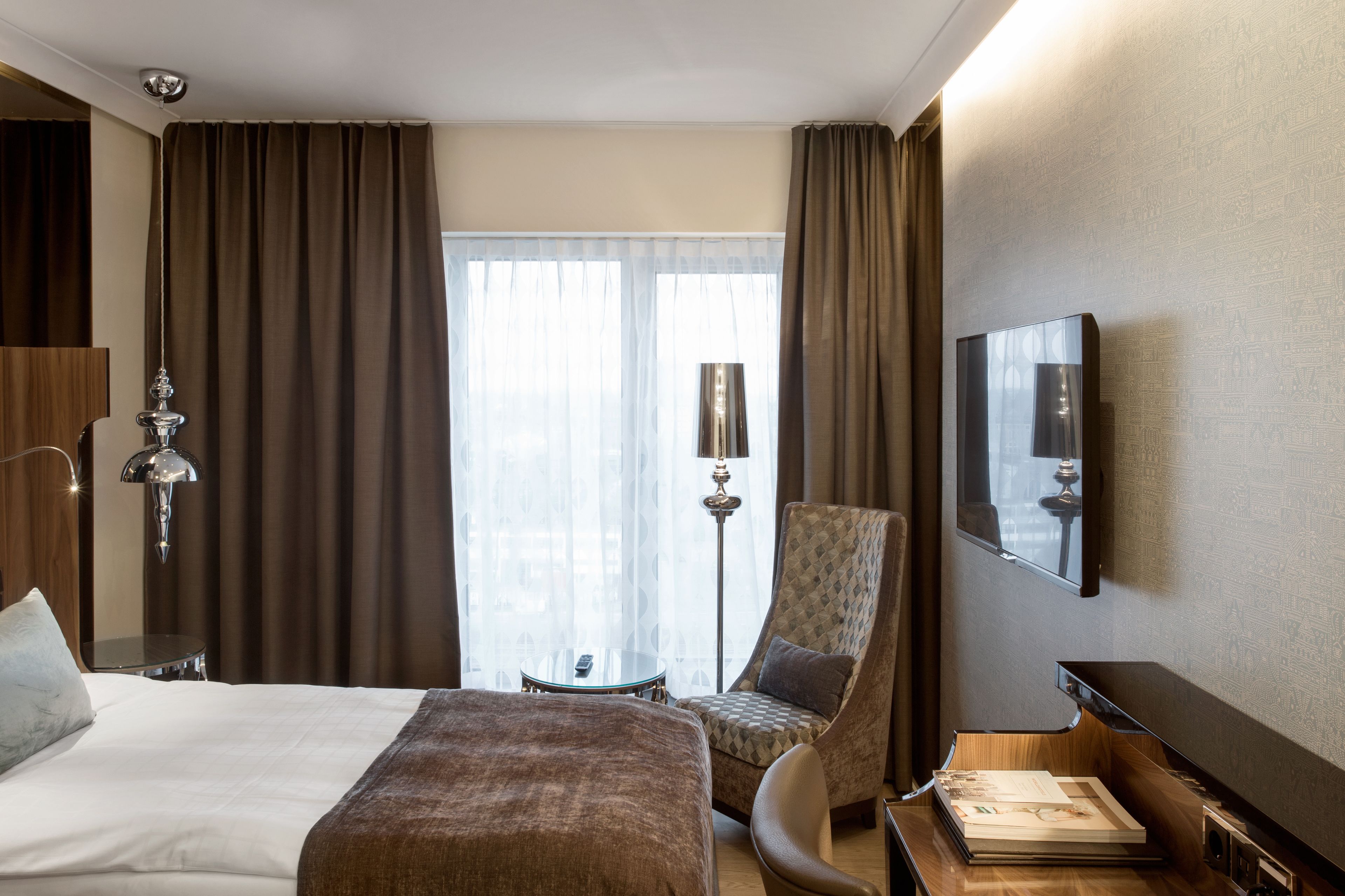 A hotel room with a large bed, a chair, a desk, a television, and a window with curtains.