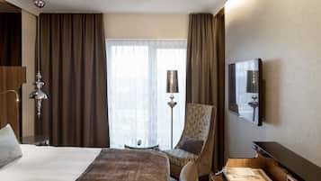 A hotel room with a large bed, a chair, a desk, a television, and a window with curtains.