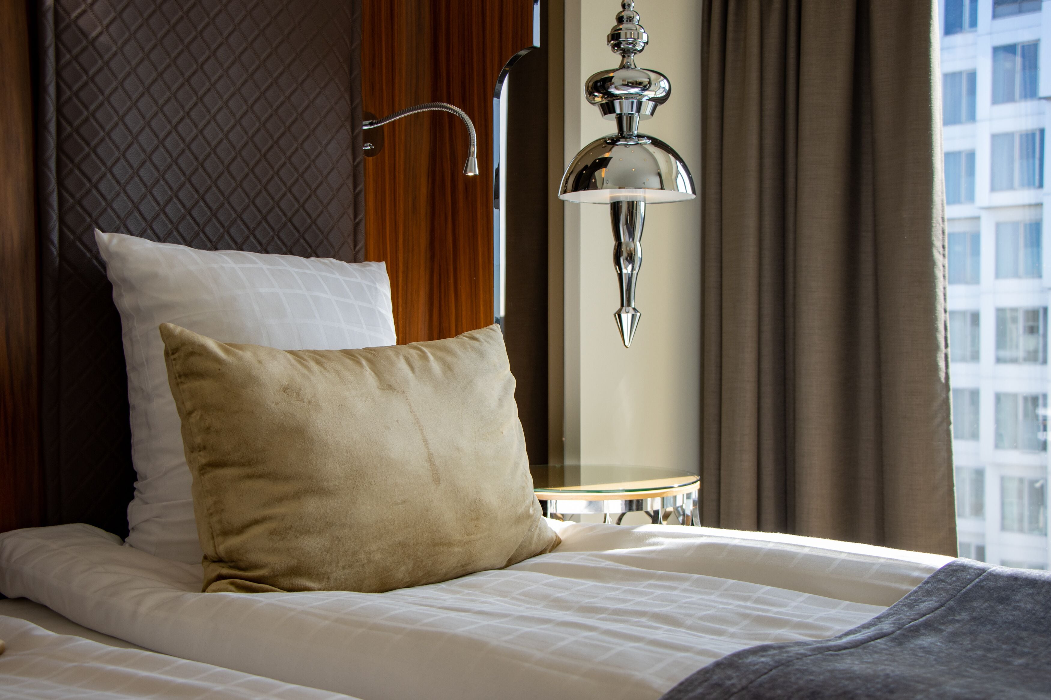 Habitación de hotel con cama, mesita de noche, lámpara y vista a un edificio desde la ventana.