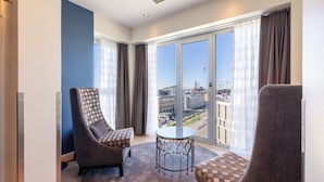A modern hotel room with two armchairs, a small table, and a large window offering a city view.
