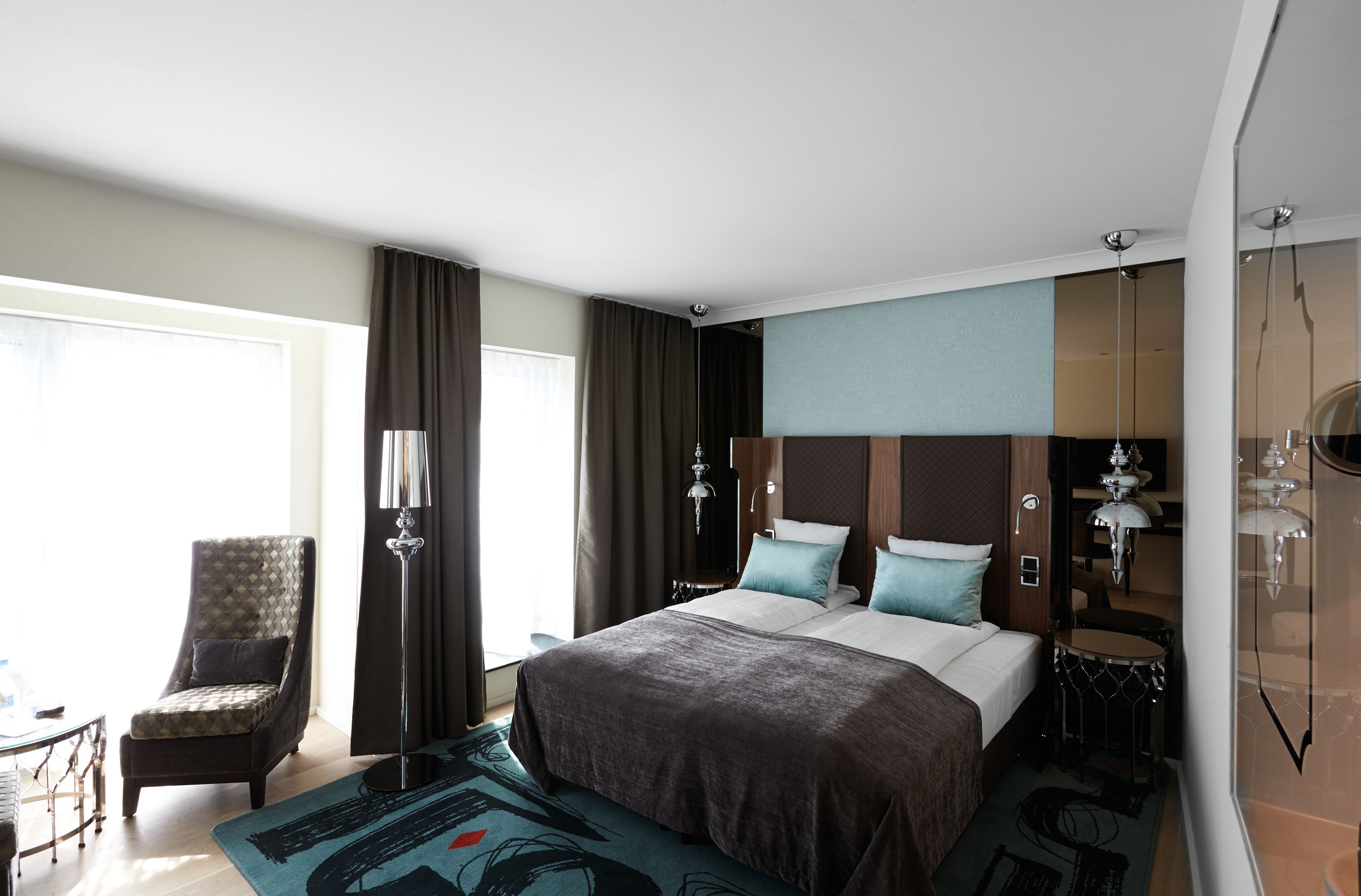 A modern hotel room with a large bed, a chair, a desk, and a view of the outdoors.