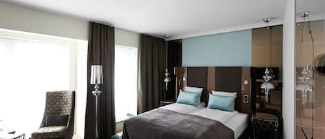 A modern hotel room with a large bed, a chair, a desk, and a view of the outdoors.