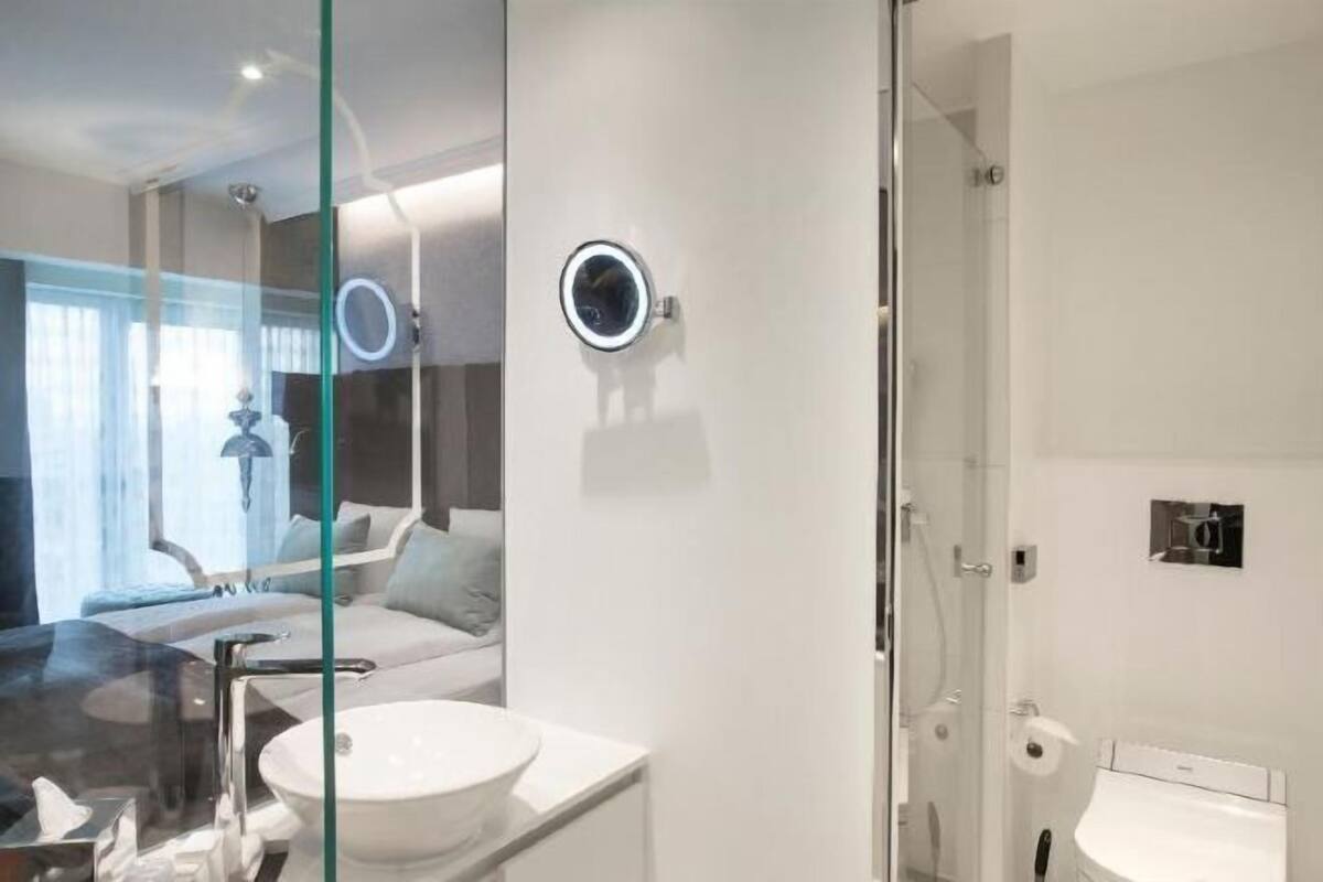 A modern bathroom with a glass shower enclosure, a round mirror, and a white sink.