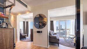 A modern living room with a round mirror, a sofa, a coffee table, and a view of the city through large windows.