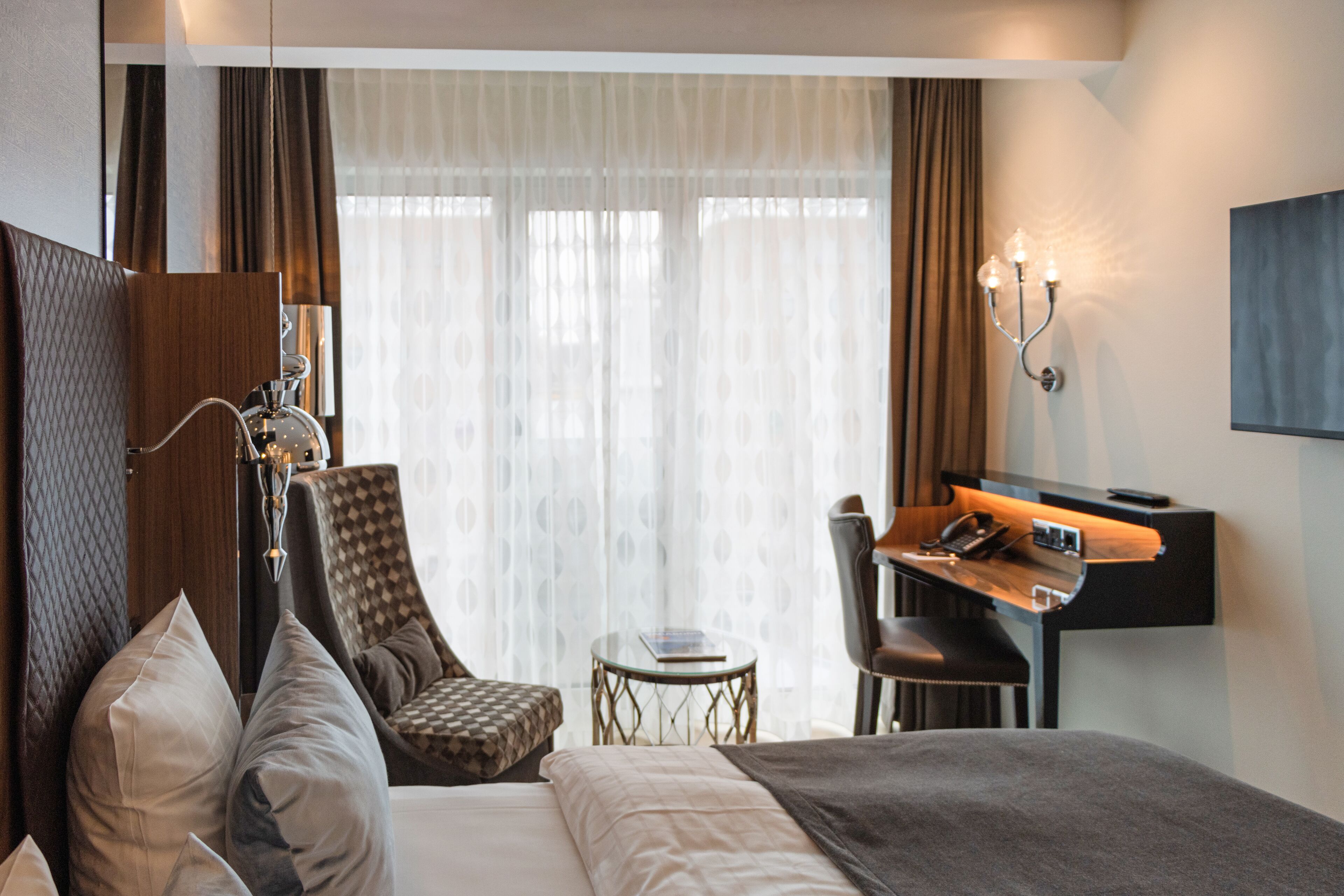 Une chambre d’hôtel avec un lit, un bureau, une chaise, une petite table et une lampe.